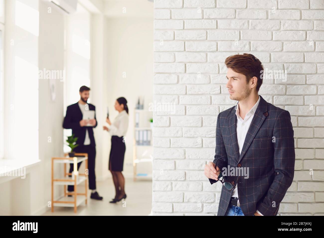 Ernsthafter Geschäftsmann in legerer Kleidung, der in einem weißen Büro an einer weißen Wand steht. Stockfoto