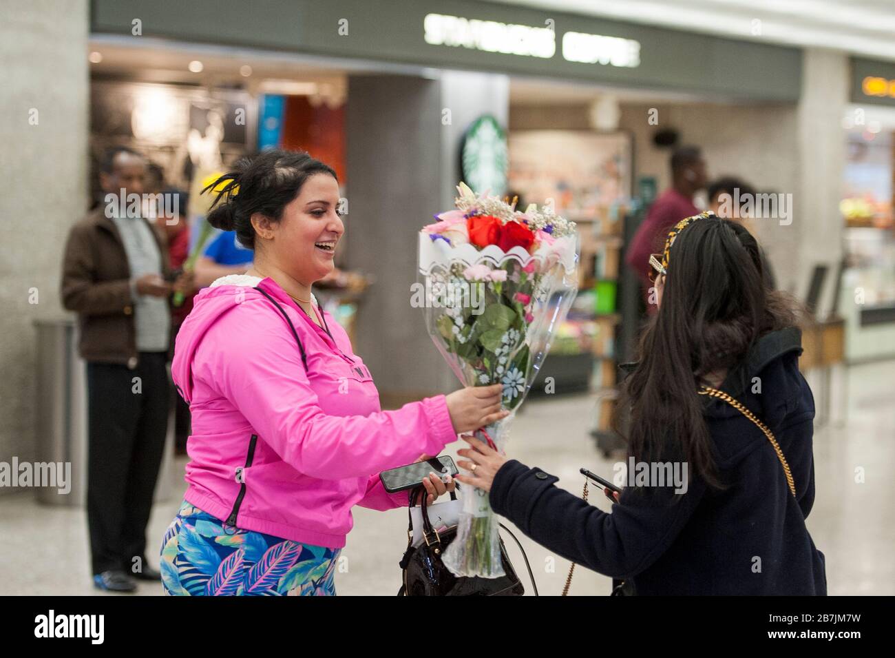 Eine Frau erhält einen Blumenstrauß, wie sie von Dubai aus nach einem 14-stündigen Flug auf Emirates-Flug 231 am internationalen Terminal am Dulles International Airport in Dulles, Virginia, Montag, 16. März 2020 ankommt. Einige Leute ergreifen die Vorsorge, Gesichtsmasken zu tragen, wenn sie ankommen, um von Familie und Freunden begrüßt zu werden. Kredit: Rod Lamkey/CNP /MediaPunch Stockfoto