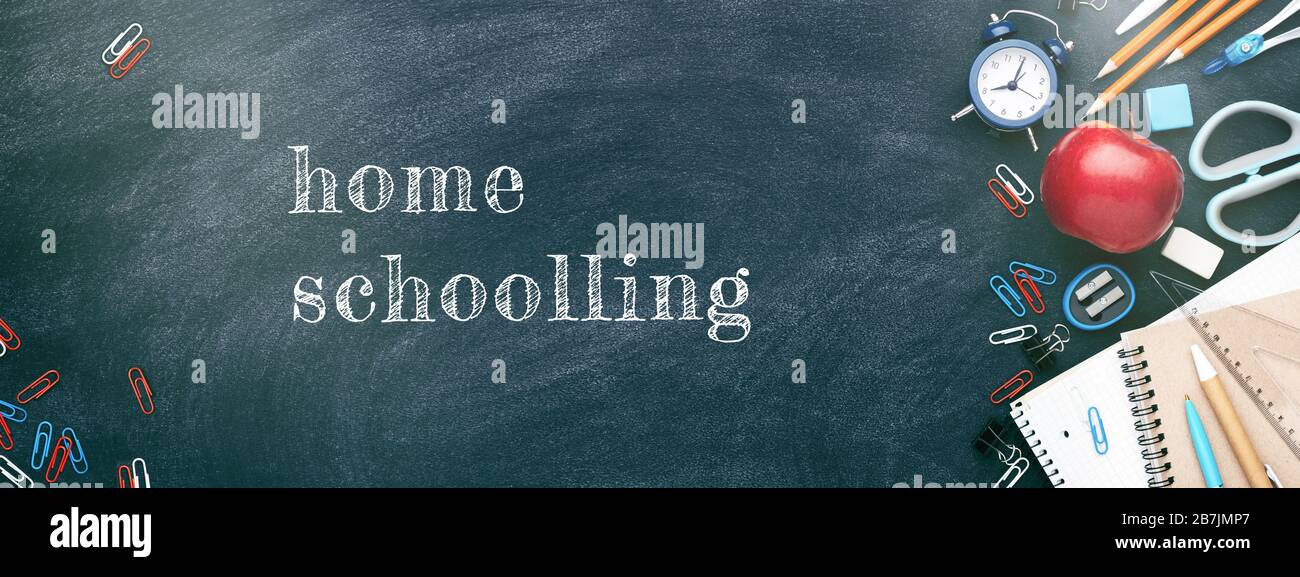 Schule stationär am Schwarzen Brett. Notizbücher, Stifte, Bleistifte, Wecker, roter apfel und andere Werkzeuge. Banner mit Aufschrift Home Schooling.. Stockfoto