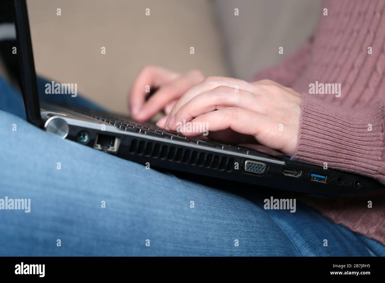 Frau in Jeans auf einer Couch mit einem Laptop auf dem Schoß sitzen. Konzept des Freiberuflers, Telearbeit von zu Hause, Online-Geschäft Stockfoto
