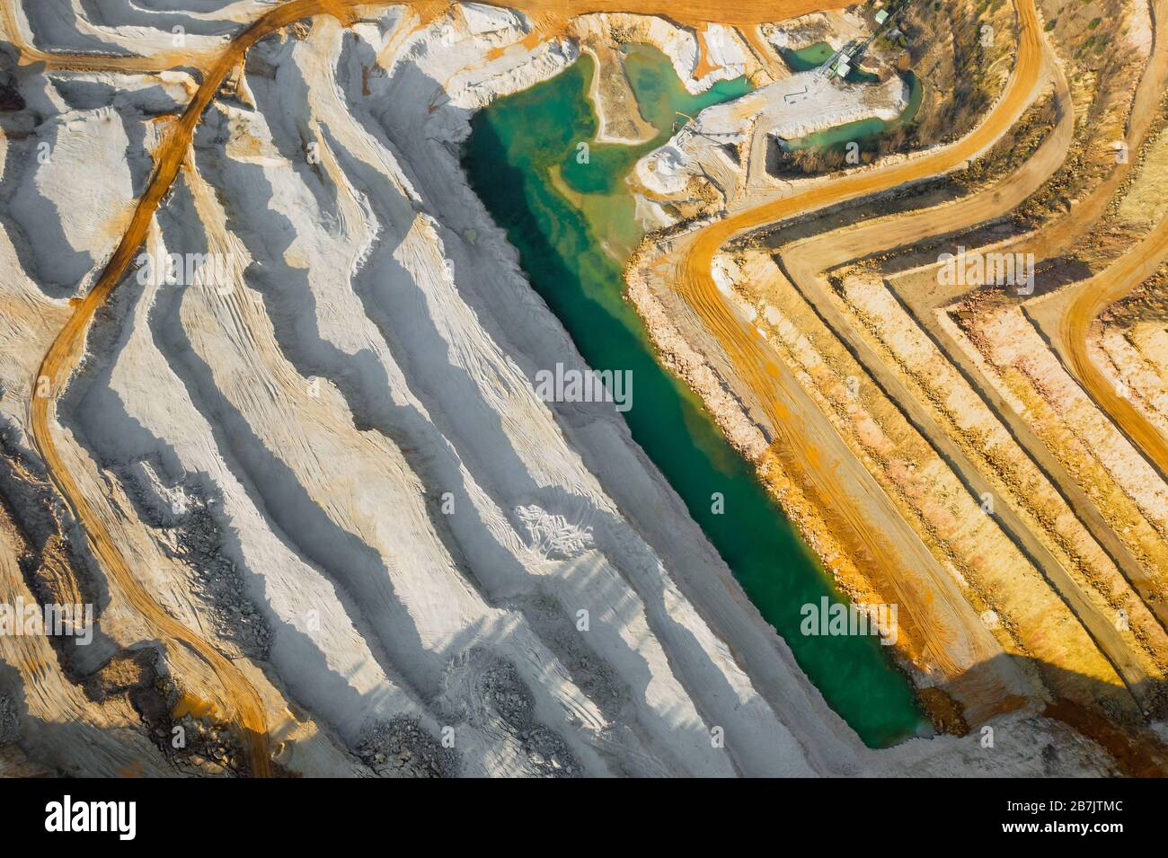 Draufsicht auf einen Sandbruch. Arial Blick auf einen Abbau von natürlichen Ressourcen oder Erz. Grüner Fluss trennt weiße und gelbe Sandufer. Stockfoto