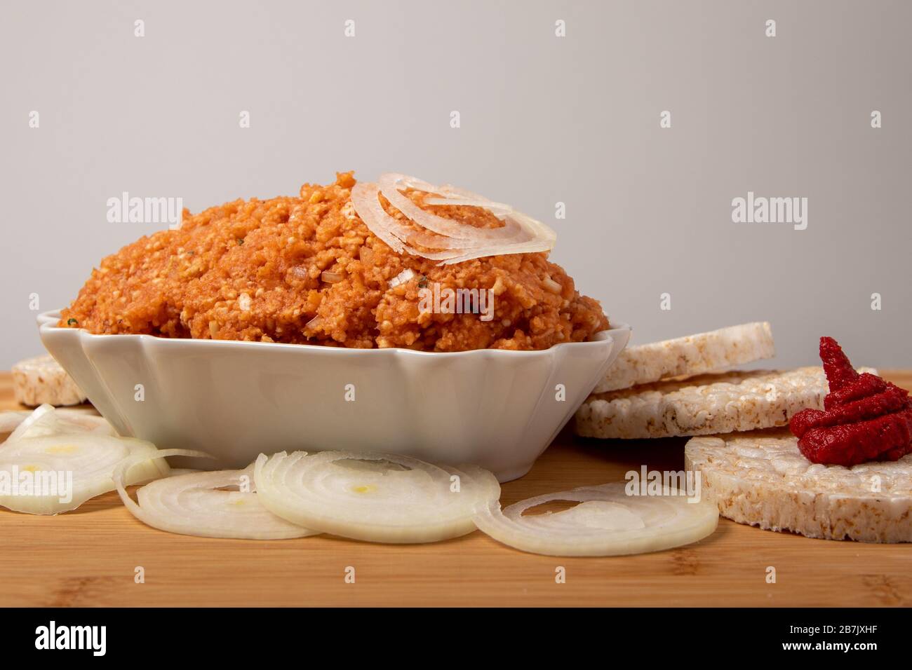 Vegane Zwiebeln, umgeben von Reiskracker, Zwiebeln und Tomatenmark, in einer Schüssel auf einem Holzbrett, Freitext Stockfoto