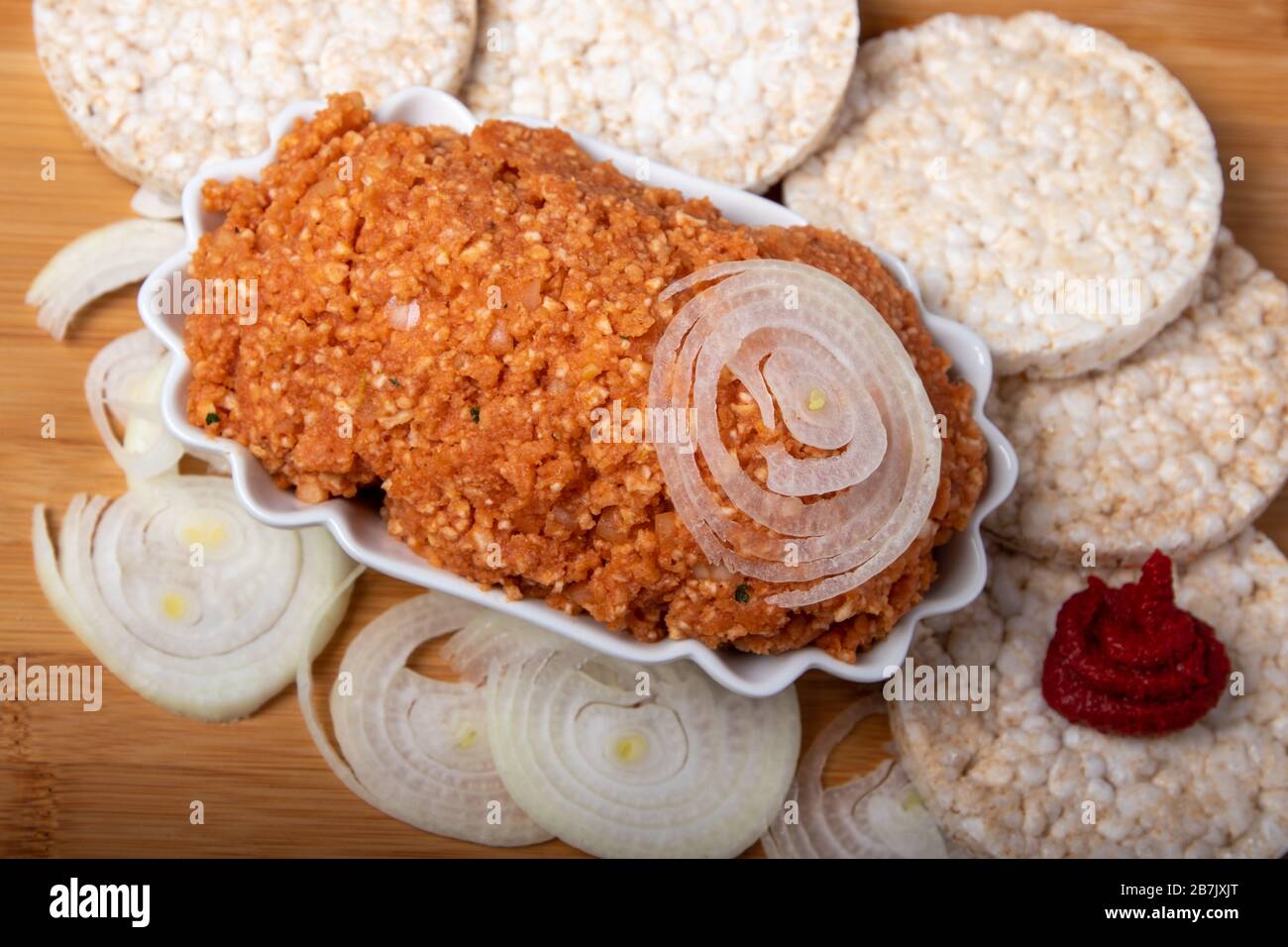 Vegane Zwiebeln, umgeben von Reiskracker, Zwiebeln und Tomatenmark, in einer Schüssel auf einem Holzbrett, Freitext Stockfoto