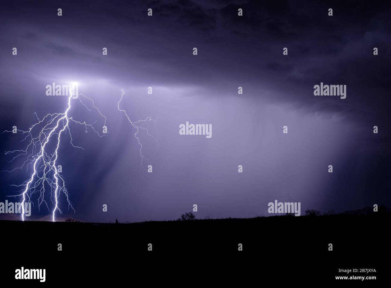 Ein heller Blitz aus Wolken erhellt einen Berg, während ein starkes Gewitter starken Regen in der Nähe von Gila Bend, Arizona, fallen lässt Stockfoto