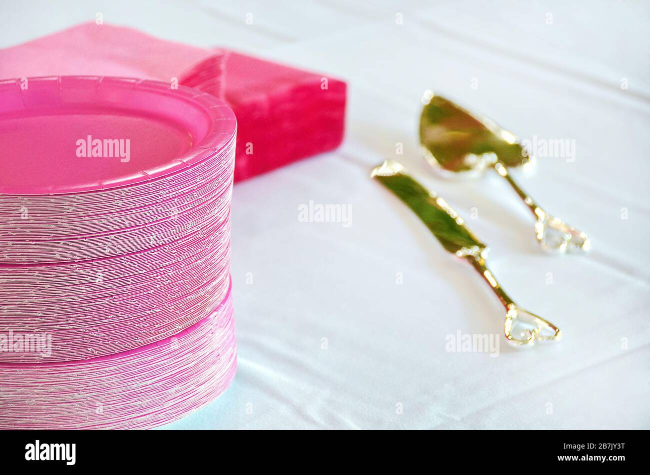 Stapel pinkfarbener Hochzeitspapierplatten mit Servietten und goldenem Geschirr auf weißem Leinentisch Stockfoto