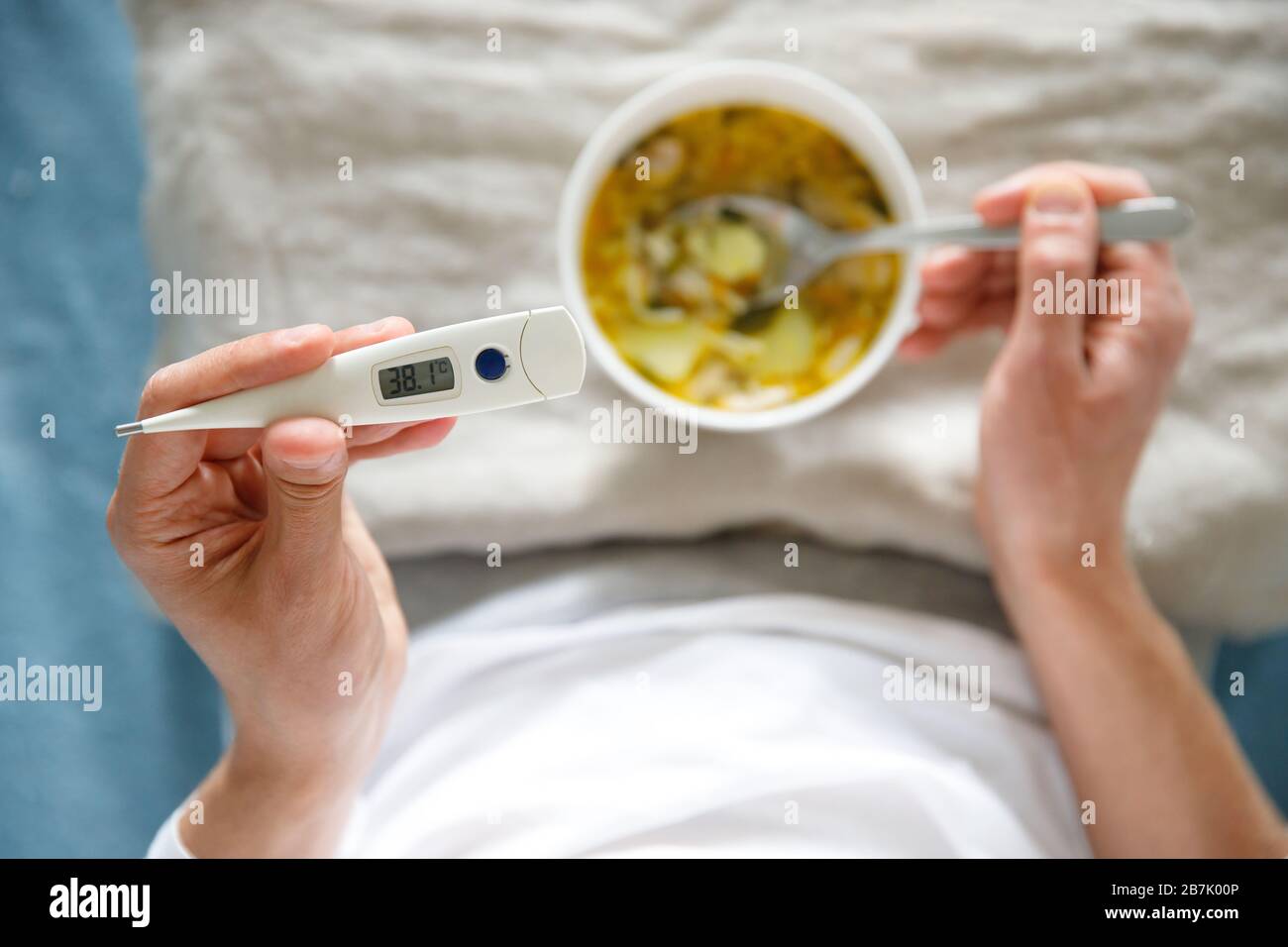 Ansicht von oben erkrankte Männer, die gesunde Hühnersuppe essen, um die Grippekrankheit zu bekämpfen, digitales Thermometer in der Hand halten, weicher Fokus. Stockfoto