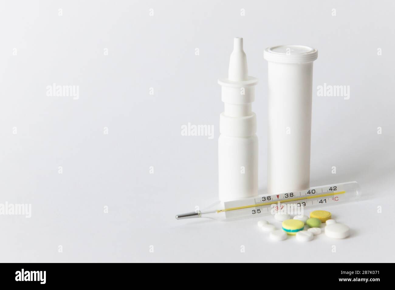 Nahaufnahme der nasalen Spritzmedizin, der weißen Pillenflasche, der bunten Pillen und des medizinischen Quecksilberthermometers, isoliert auf weißem Hintergrund mit Kopierraum. Grippe, Stockfoto