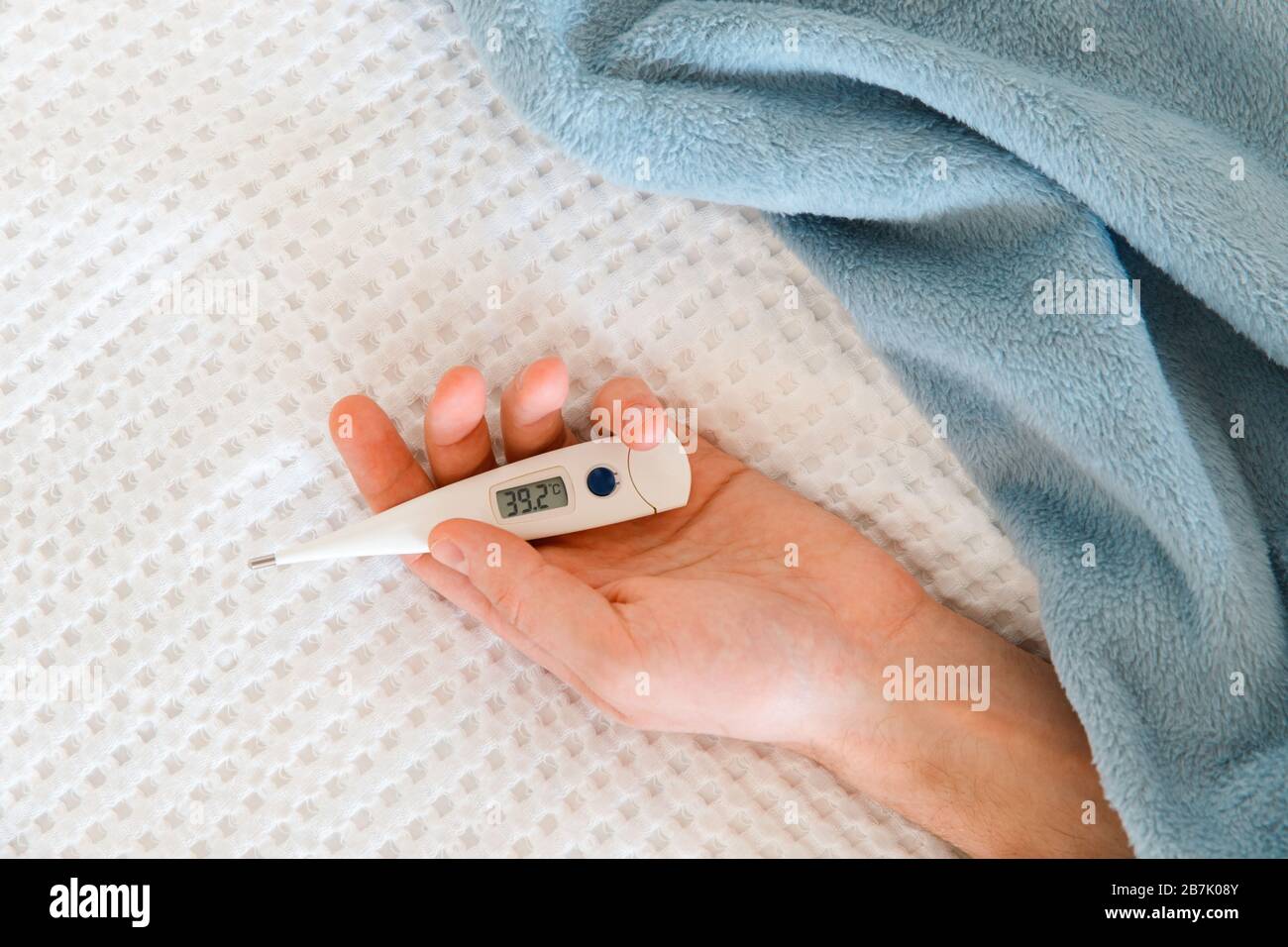 Nahaufnahme der Hand des Menschen, die ein digitales Thermometer hält, das auf dem Bett liegt, im Innenbereich. Hohes Konzept für Körpertemperatur, Kälte und Grippeepidemie Stockfoto