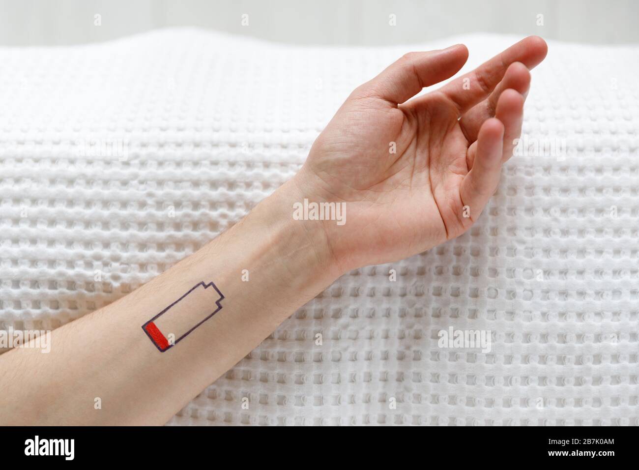 Symbol für niedrigen Batteriestand auf der menschlichen Hand. Müde Mann auf dem Bett liegend, Draufsicht. Überarbeit, erschöpft, Lebensenergie Konzept. Stockfoto