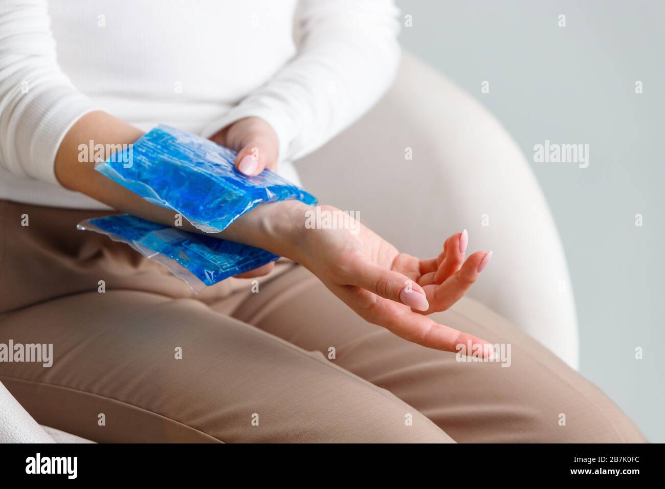 Nahaufnahme der Frau, die eine kalte Kompression auf ein schmerzhaftes Handgelenk anwendet, das durch längere Arbeit am Computer, Laptop, verursacht wird. Karpaltunnelsyndrom, Arthritis, n Stockfoto