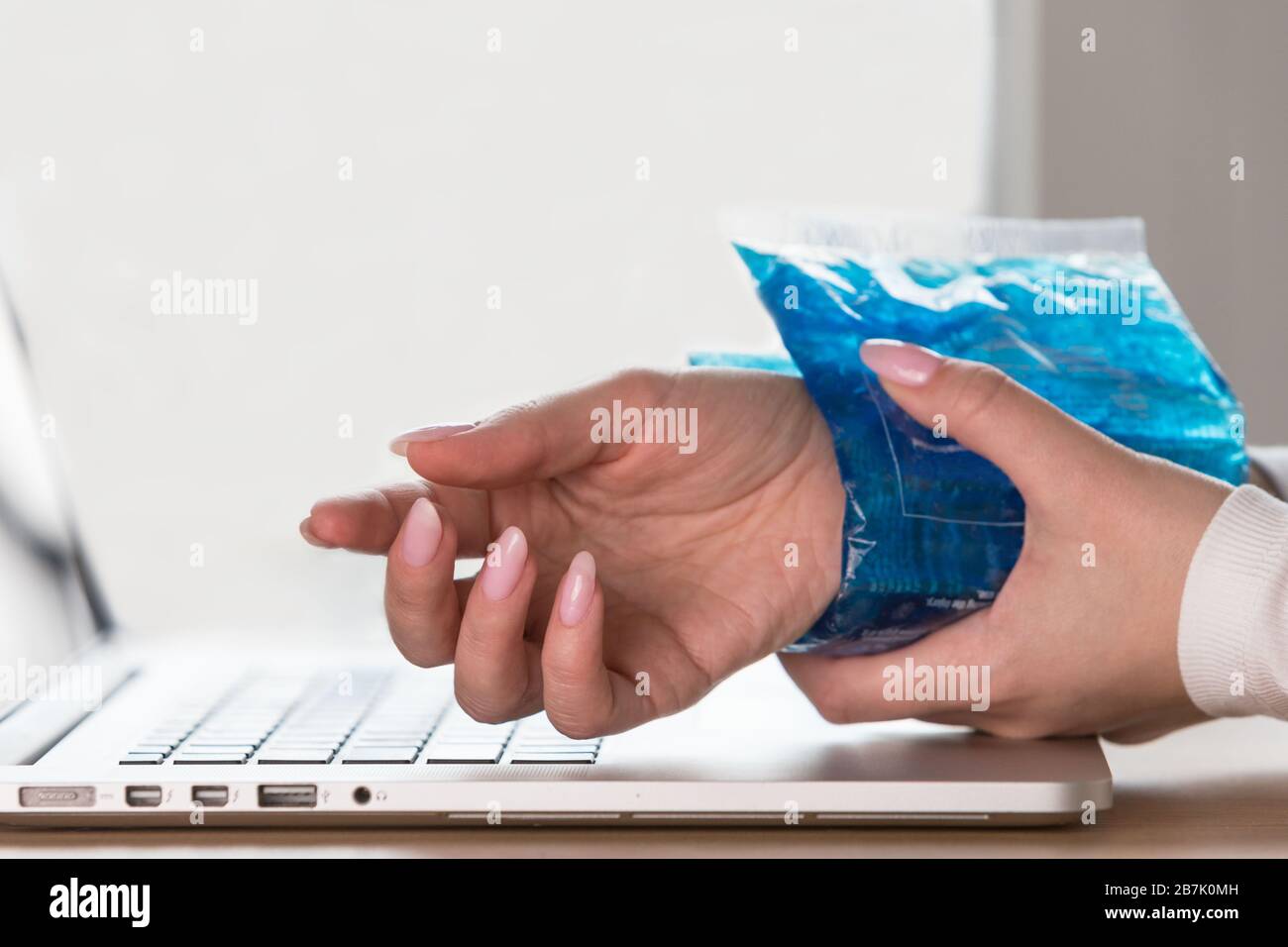Nahaufnahme der Frau, die eine kalte Kompression auf ein schmerzhaftes Handgelenk anwendet, das durch längere Arbeit am Computer, Laptop, verursacht wird. Karpaltunnelsyndrom, Arthritis, n Stockfoto