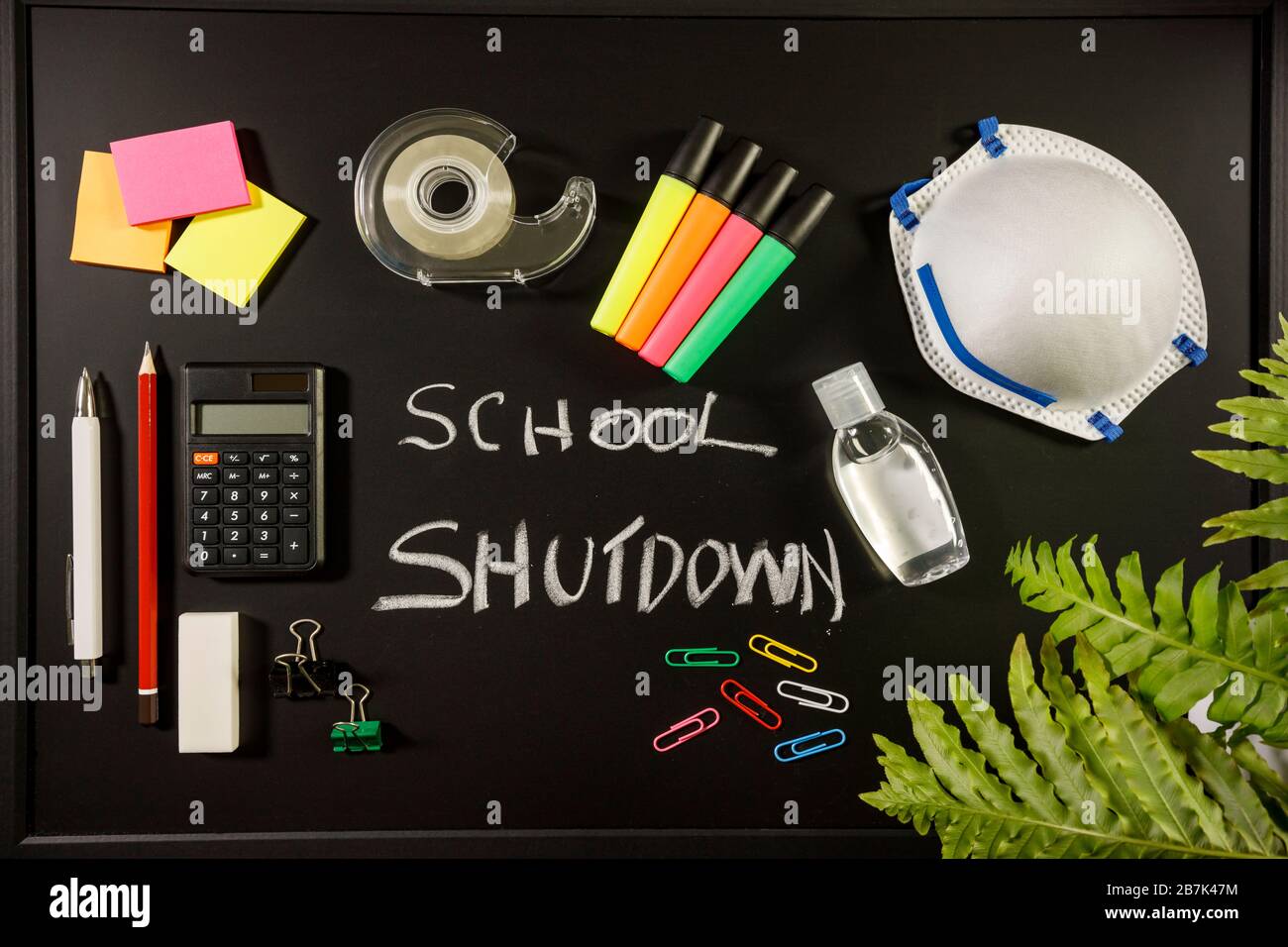 Caronavirus Schulabschaltung Konzept mit persönlicher Maske, Handdesinfektionsmittel und Schreibwaren auf schwarzem Flachlay, Schulabschaltung mit Kreide-Draufsicht geschrieben Stockfoto