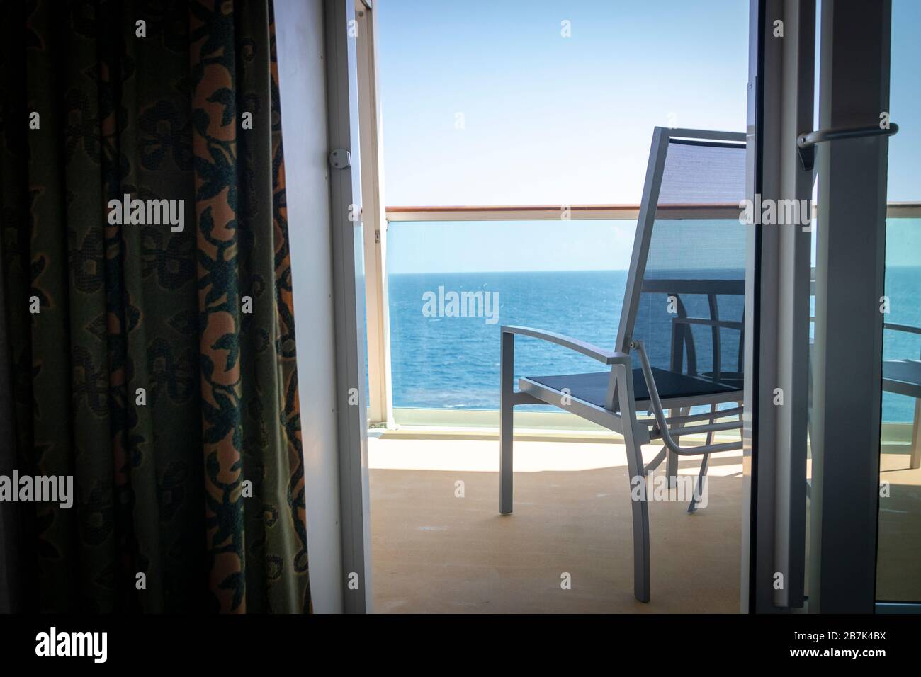 Blick auf den leeren Terrassenstuhl und den Balkon des Kreuzfahrtschiffs oder des Ferienimmobilienraums mit Blick auf das blaue Meerwasser Stockfoto