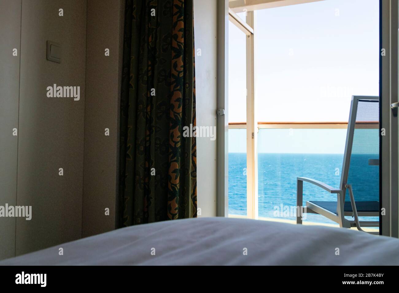 Blick auf den leeren Terrassenstuhl und den Balkon des Kreuzfahrtschiffs oder des Ferienimmobilienraums mit Blick auf das blaue Meerwasser Stockfoto