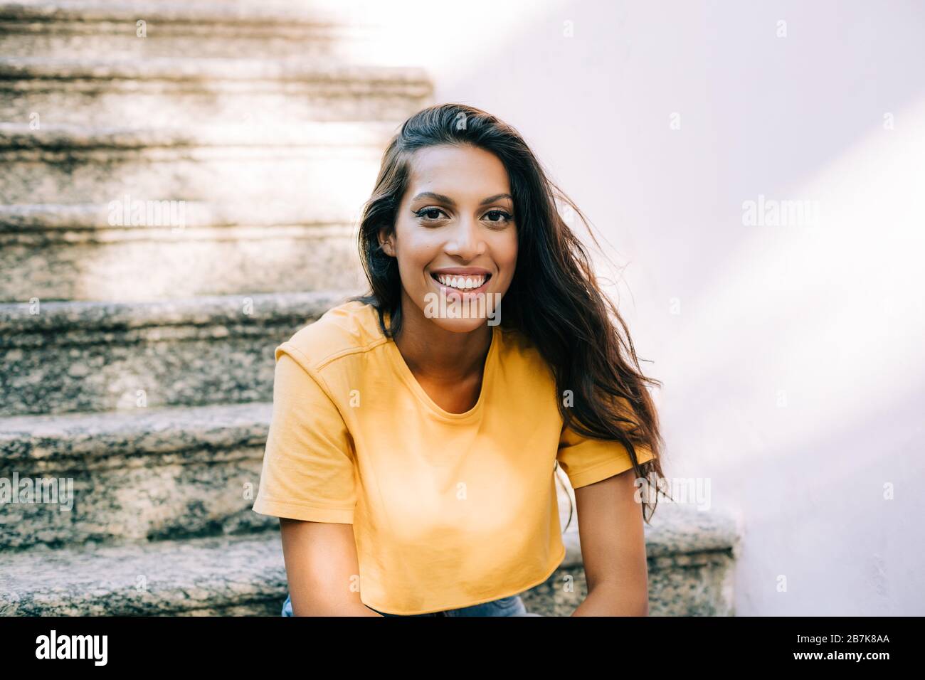 Bild eines latinamerikanischen Mädchens, das lächelnd auf der Treppe sitzt Stockfoto