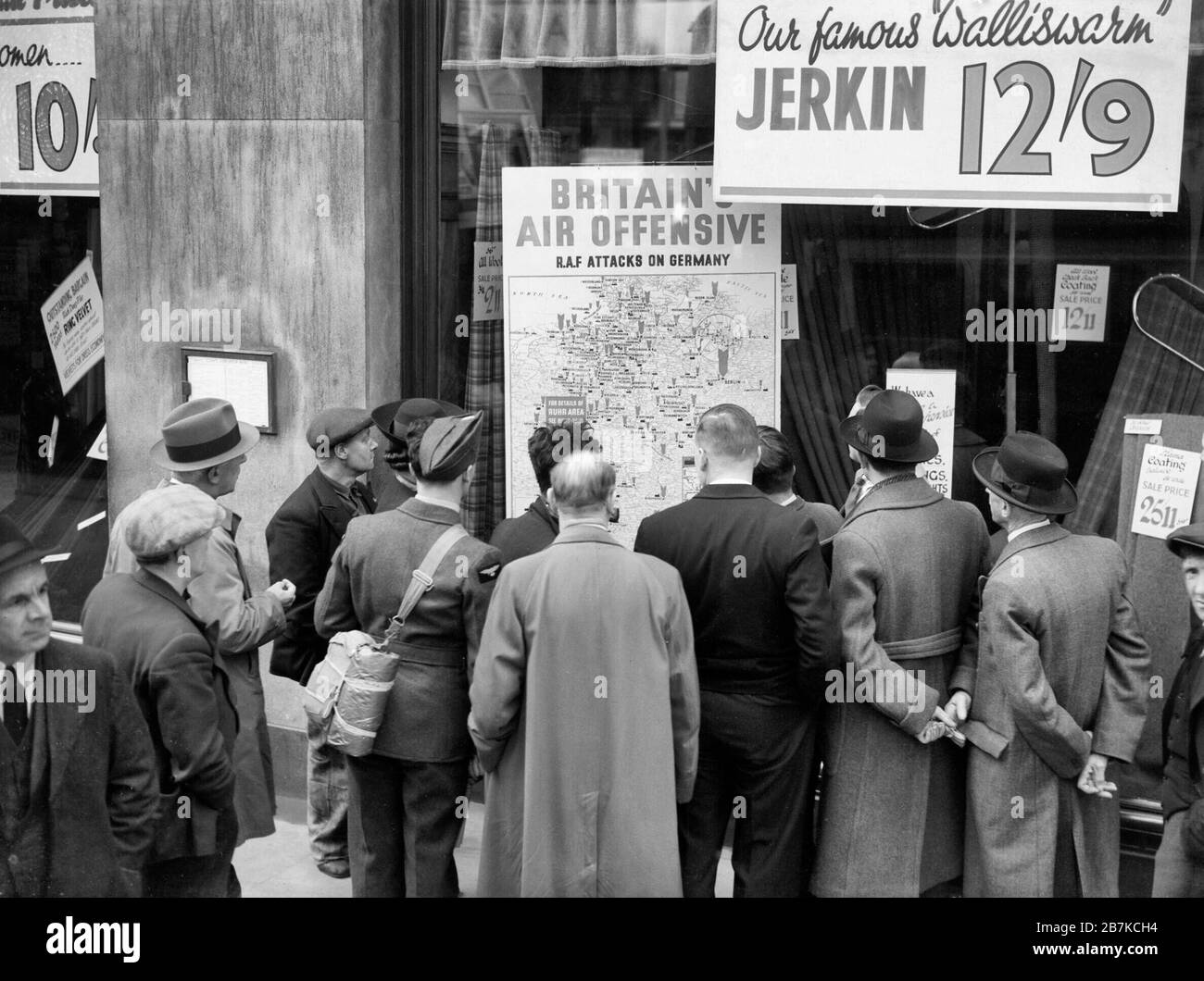 Ein britischer Flieger gehört zu einer Gruppe von Zivilisten, die sich um das Fenster eines Ladens in Holborn, London, drängen, um sich eine Karte anzusehen, die zeigt, wie die RAF im Jahr 1940 in Deutschland zurückschlägt. Stockfoto