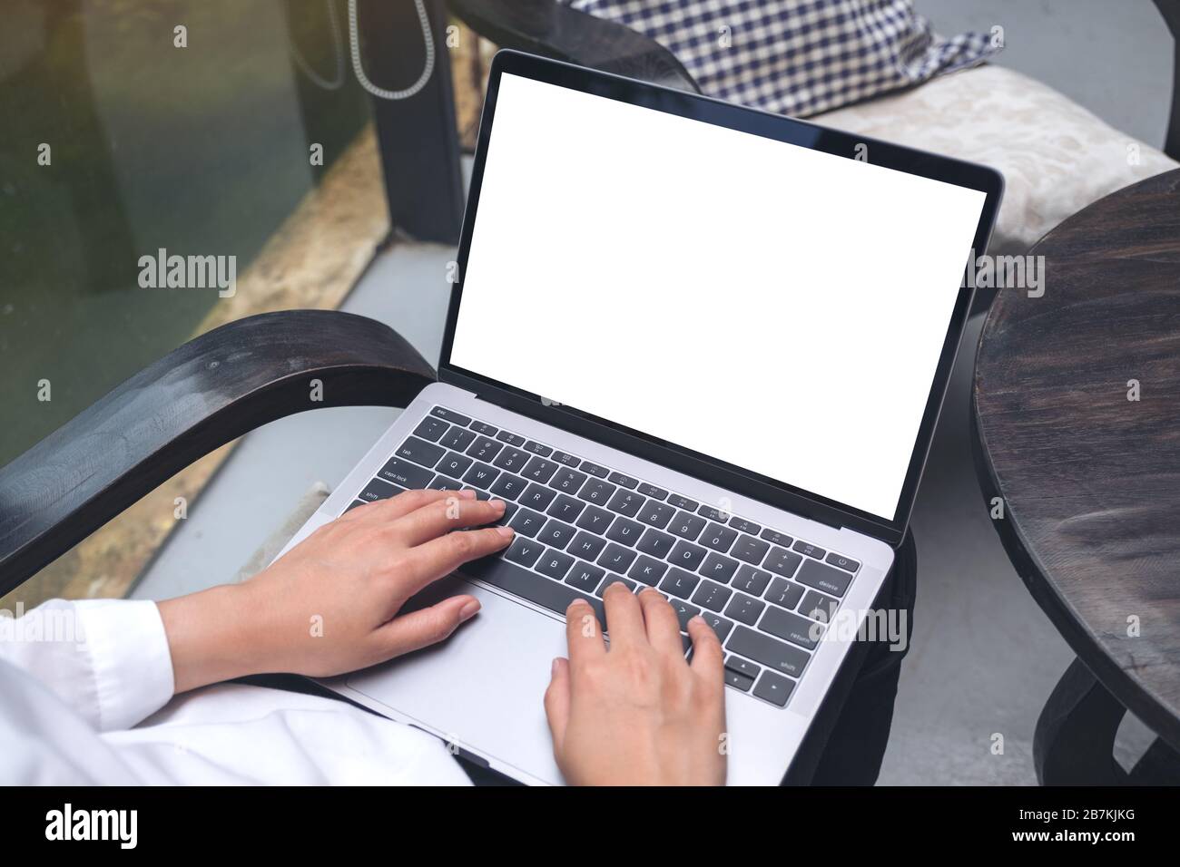 Top-View-Mockup-Bild einer Frau, die auf einem Laptop mit leerem weißem Desktop-Bildschirm tippt und dabei auf einem Stuhl sitzt Stockfoto