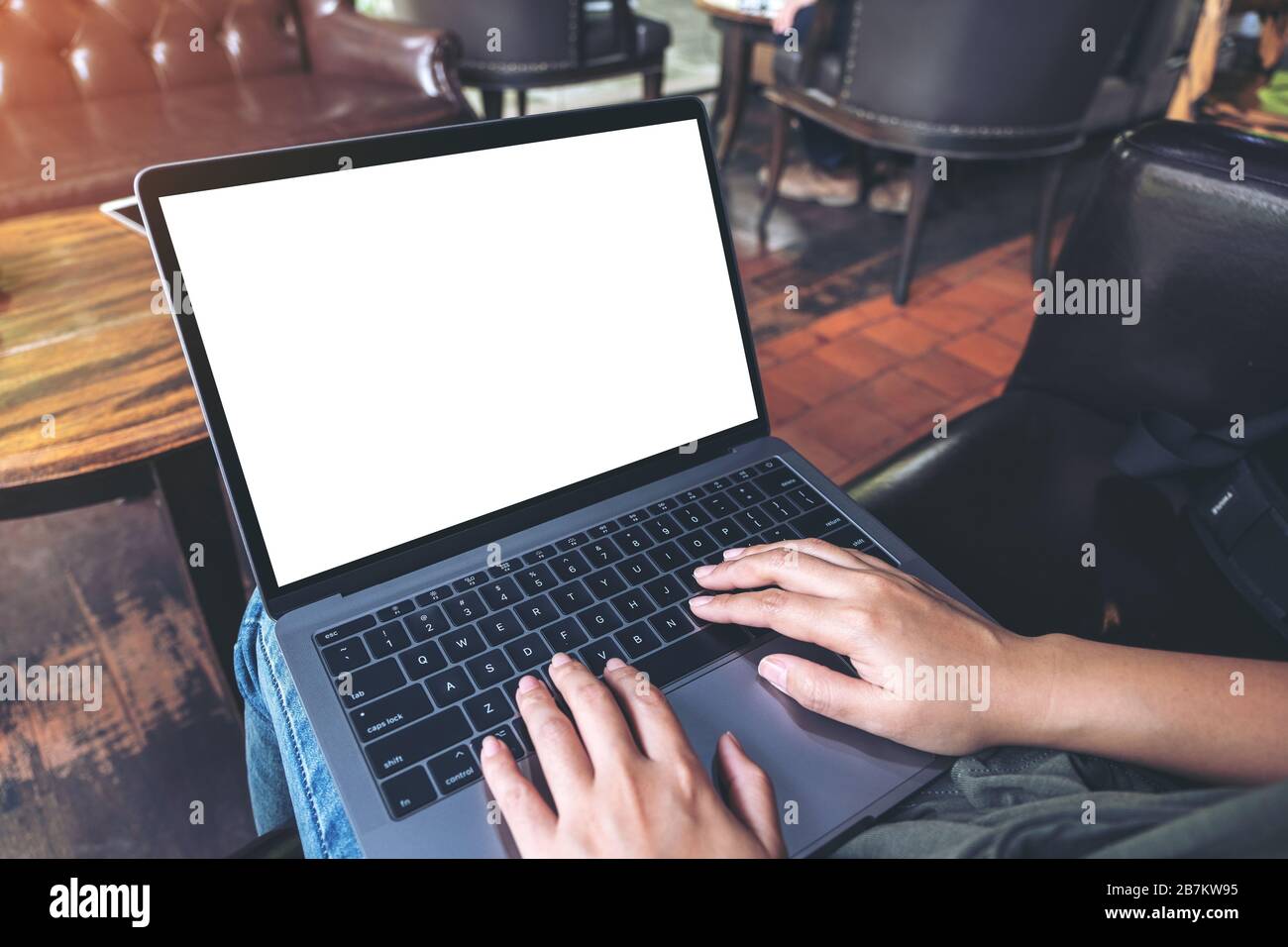 Mockup-Bild einer Frau, die im Café sitzt und auf dem Laptop mit leerem weißem Desktop-Bildschirm tippt Stockfoto