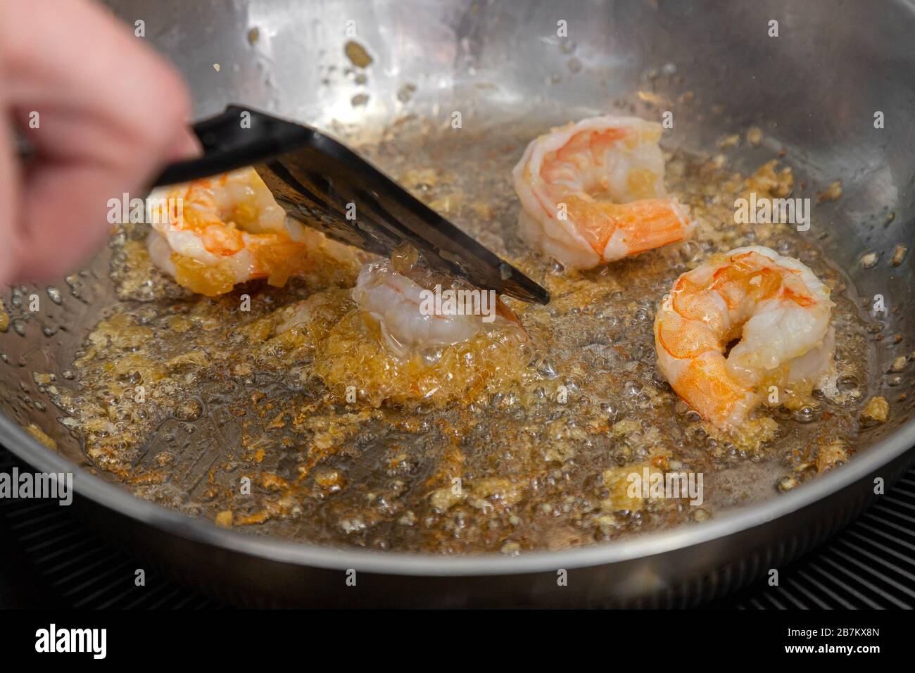 Сlose-up eines männlichen Küchenchefs, der große Garnelen in Olivenöl auf einer Metallpfanne brate. Der Prozess der Herstellung von Garnelen und Pasta Stockfoto