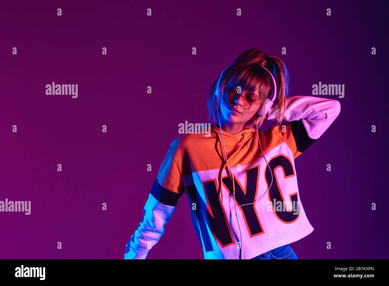 Happy Girl Wear Brille Kopfhörer hören Tanzmusik im violetten Hintergrund. Stockfoto