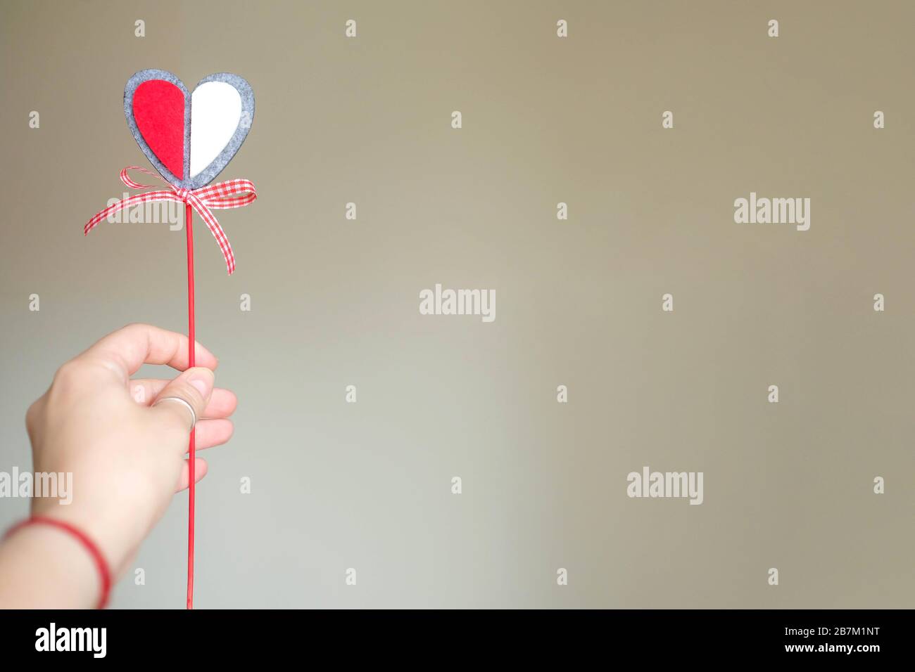 Halten Sie ein dekoratives Herz an einem Stock in der Hand. Im Hintergrund ein homogener Hintergrund. Valentinstag. Stockfoto