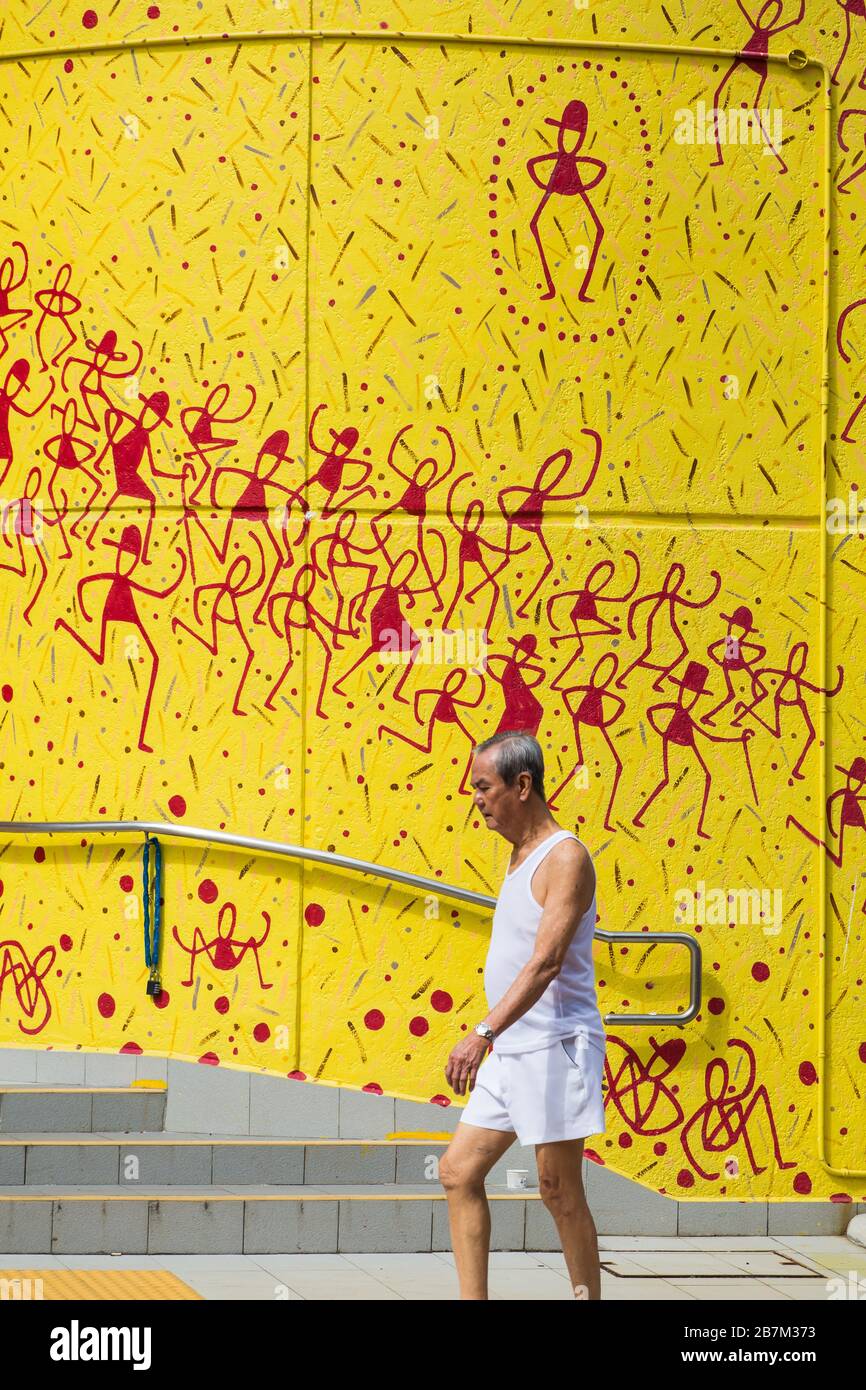Ein alter chinesischer Mann in weißem Singlet läuft über ein gelbes Wandmuster in Chinatown, Singapur Stockfoto