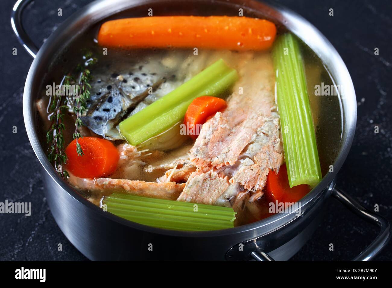 Fischbrühe oder Suppe aus Lachs, Zwiebel, Karotte, Sellerie, Kräutern und Gewürzen in einem Vorratsbehälter auf einem Betontisch, in der Nähe Stockfoto
