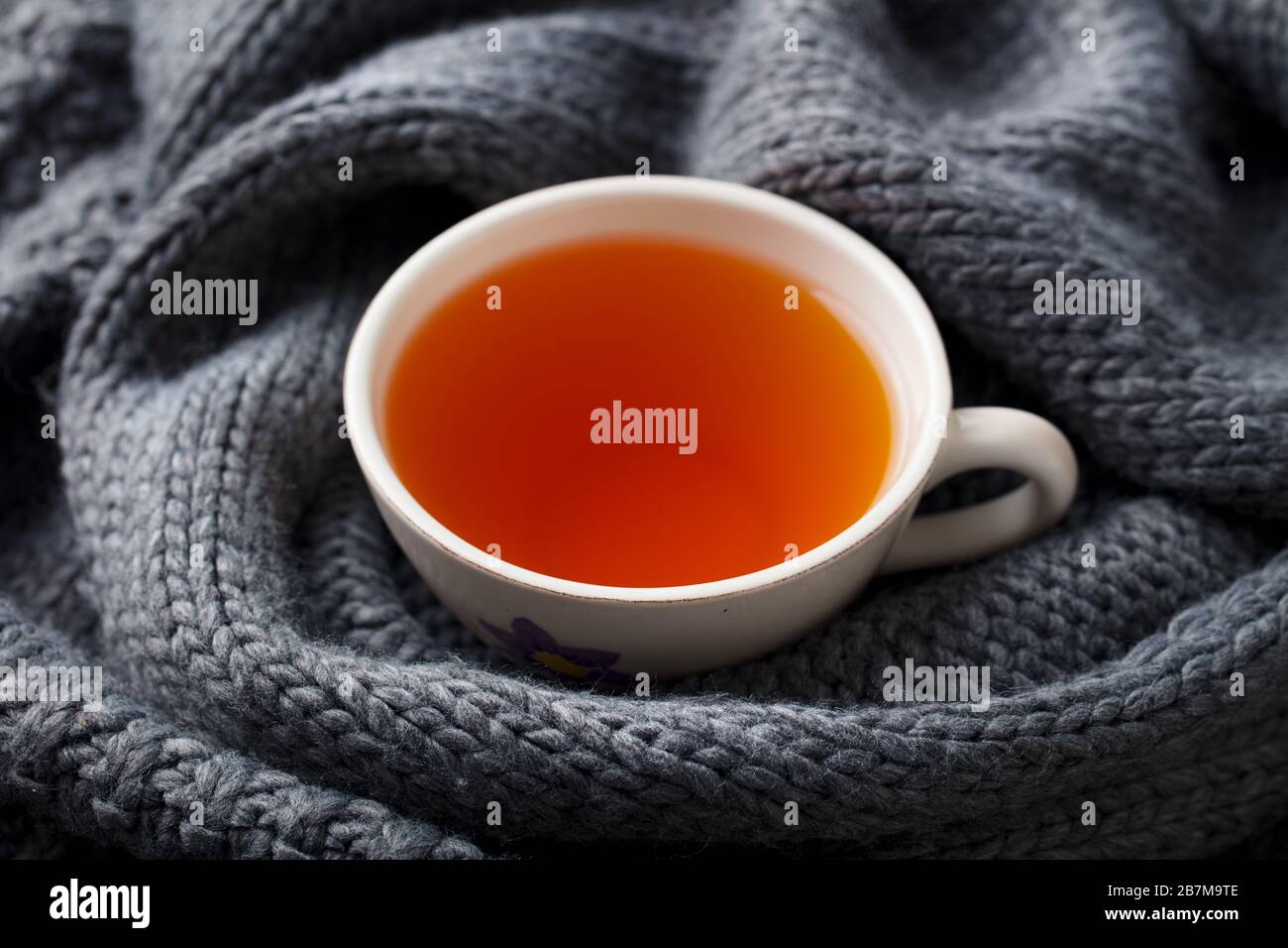 Tasse Tee. Grau gestrickter Schal Hintergrund. Nahaufnahme. Stockfoto