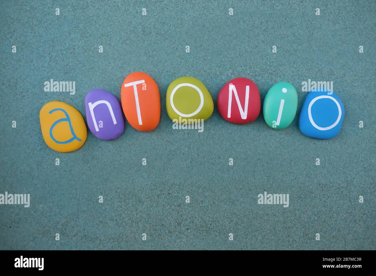 Antonio, lateinischer Männername, der mit mehrfarbigen Steinbuchstaben über grünem Sand besteht Stockfoto