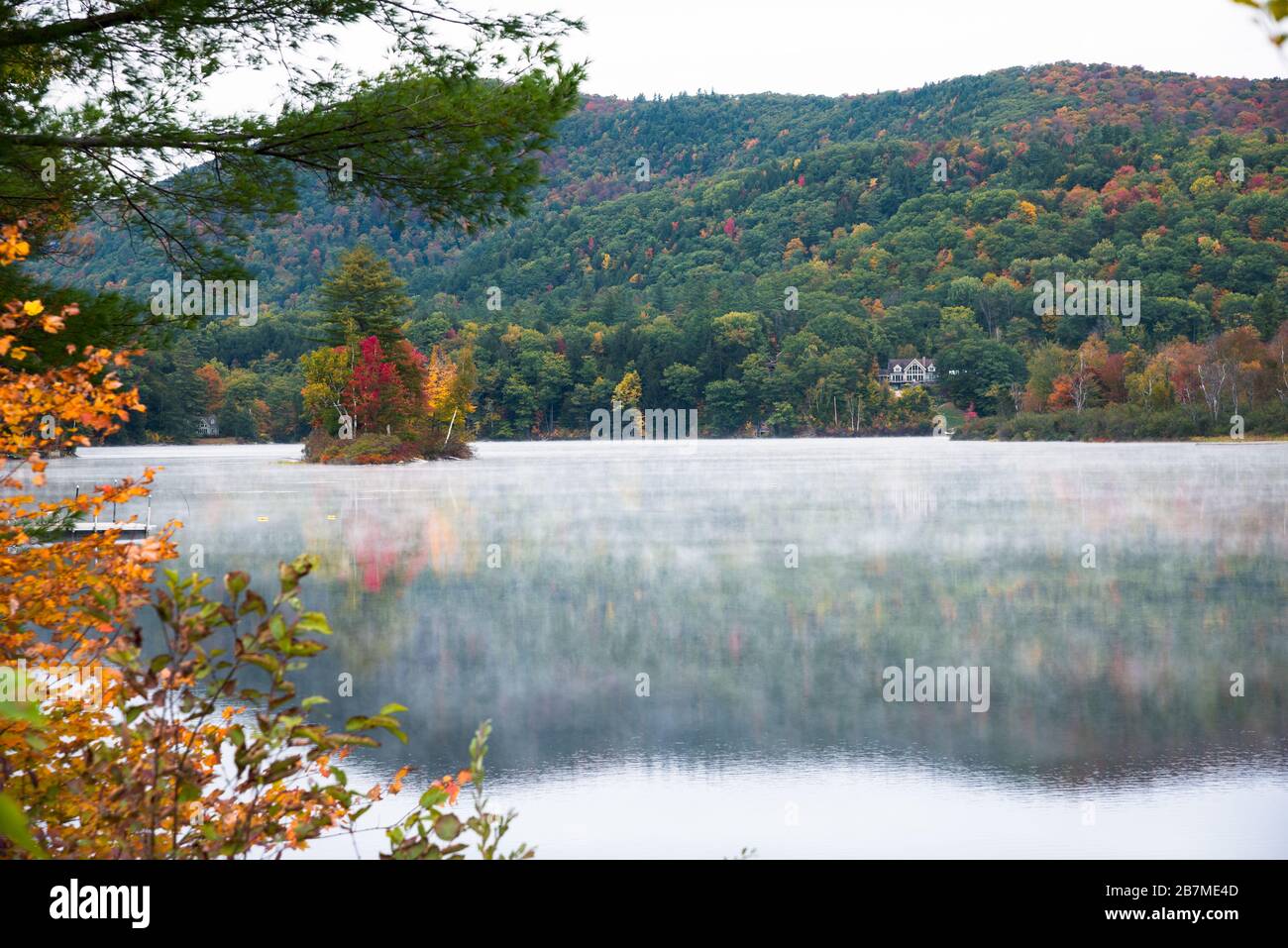 Der von bewaldeten Hügeln umgebene See mit Morgennebel bedeckt das Wasser im Herbst Stockfoto