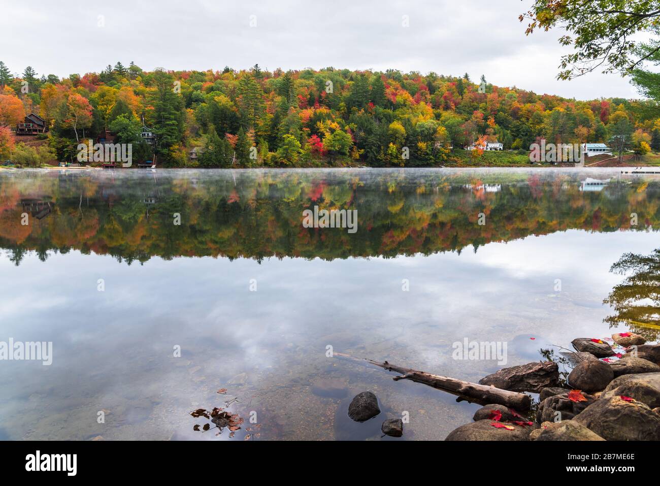 Bergsee mit Ferienhäusern am bewaldeten Ufer während der Herbstfarbsaison Stockfoto