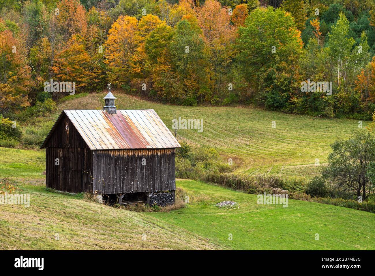 Holzhütte in einem von farbenfrohem Herbstwald überfluteten Medow in einer rollenden ländlichen Landschaft Stockfoto