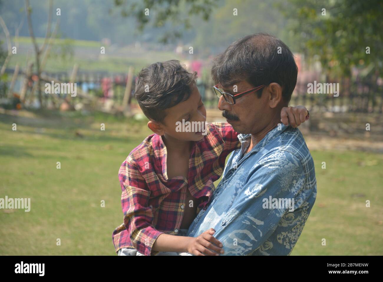 Nahaufnahme eines Mannes, der einen jungen Jungen in der Nähe seiner Brust hält, Runde mit Brille in einem Park, selektive Fokussierung Stockfoto