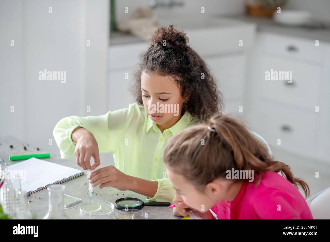 Zwei Mädchen sitzen am Tisch und führen ein Experiment durch. Stockfoto