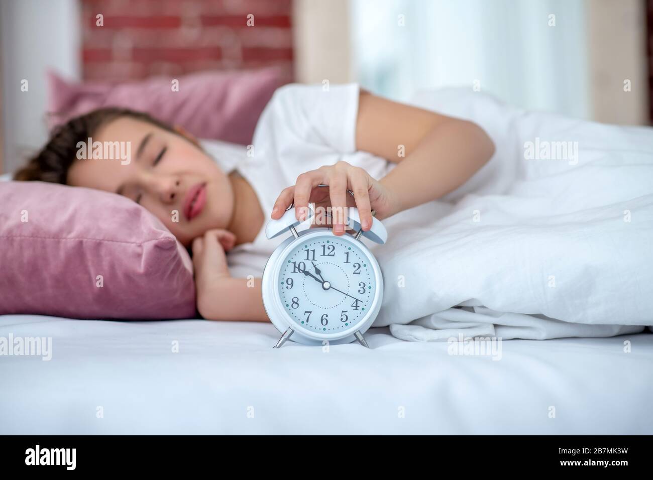 Schlafendes Teenager-Mädchen im Bett, Hand auf den Wecker. Stockfoto