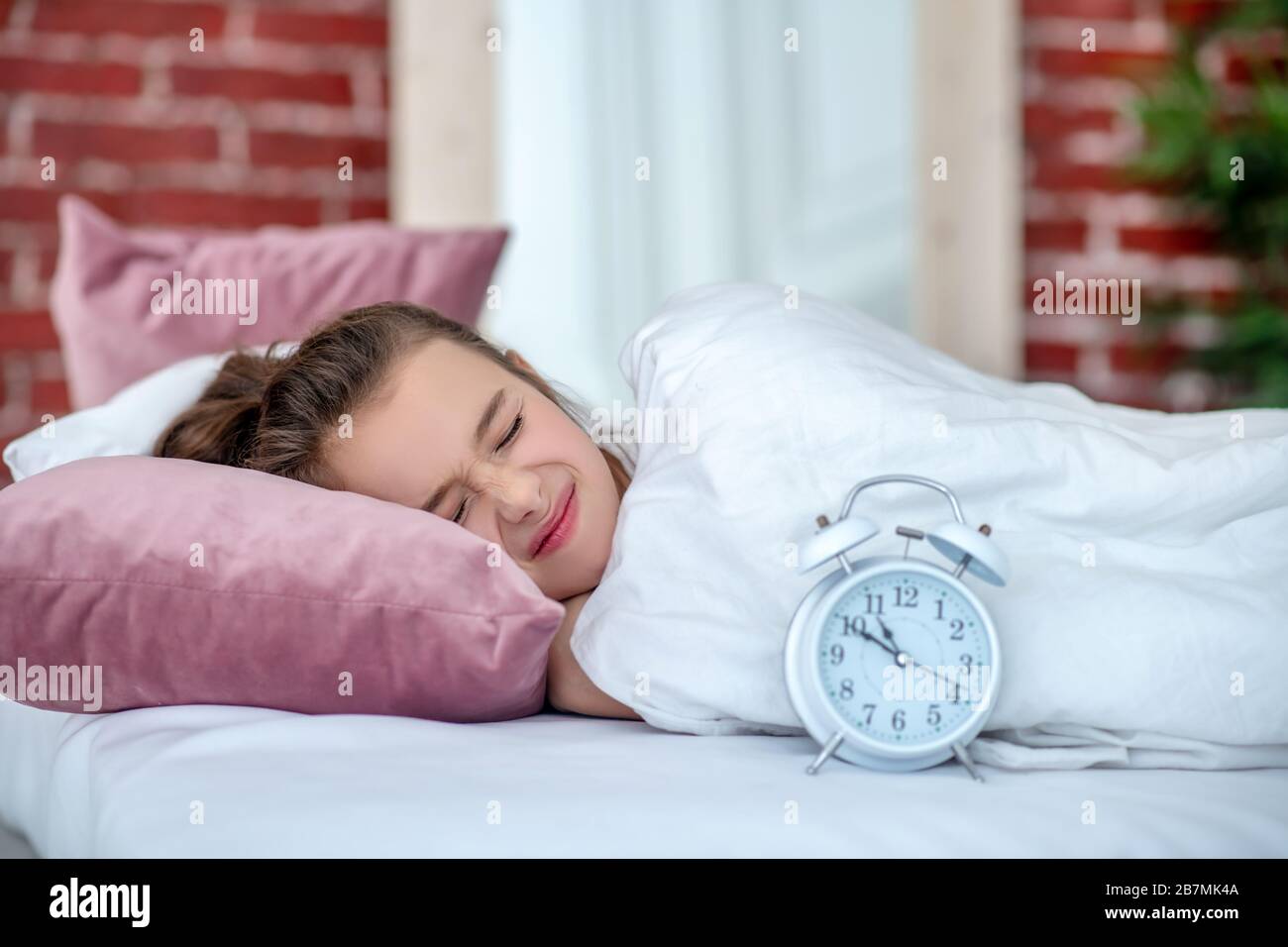 Mädchen schläft in weißem Bett, neben weißem Wecker. Stockfoto