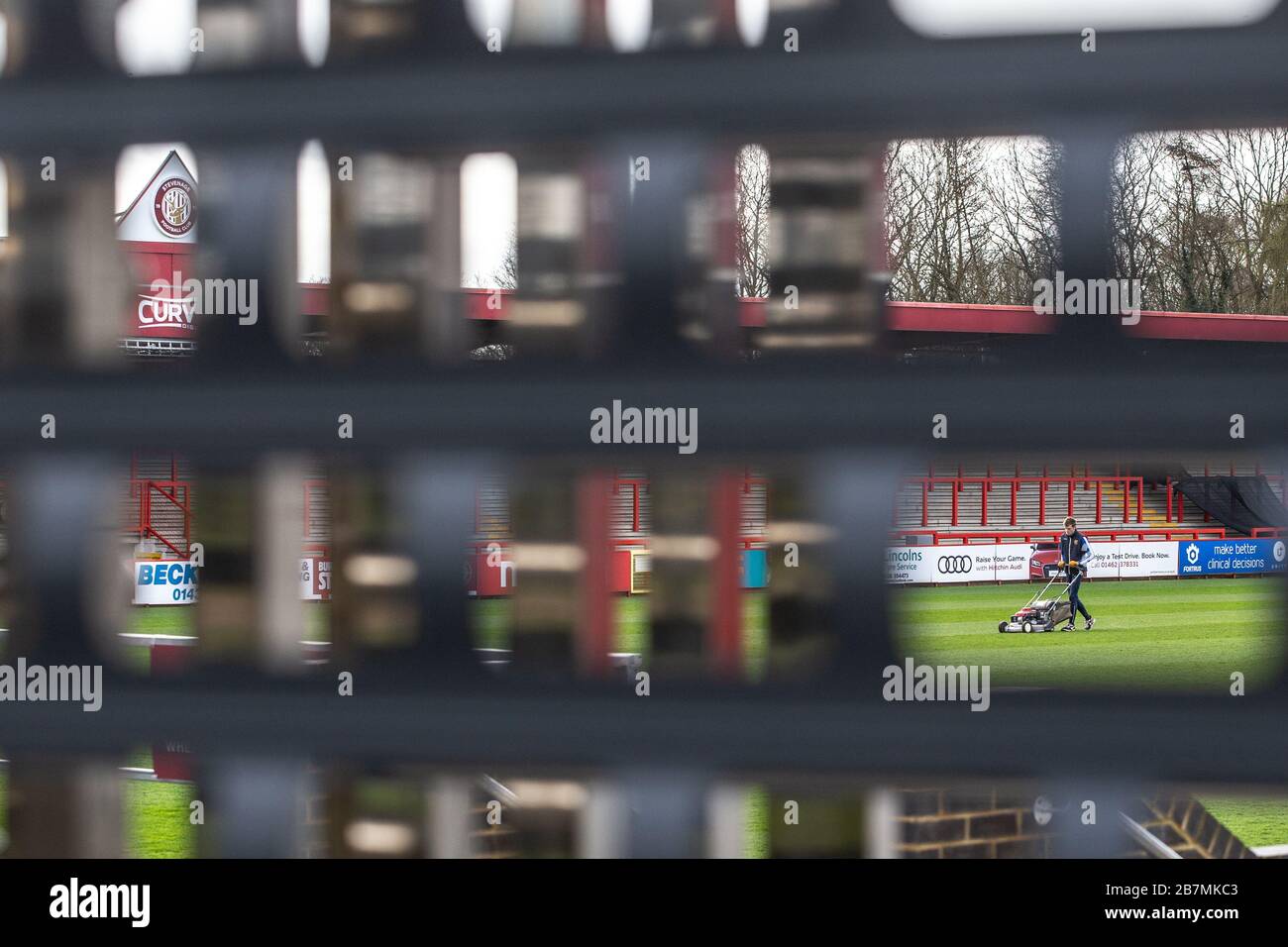 Groundsman arbeitet auf dem Fußballplatz und schneidet Gras, fotografiert durch die Lücke im geschlossenen Verschluss. Stockfoto