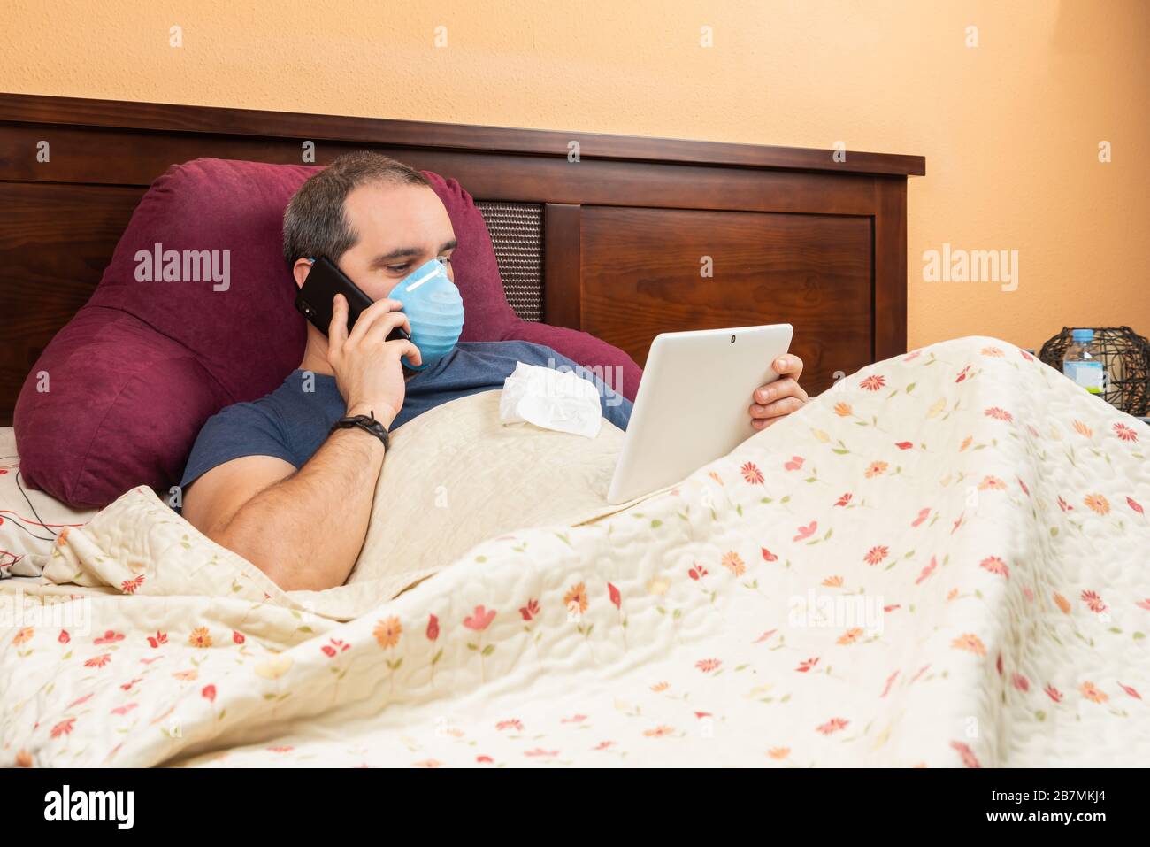 Kranker Mann mit Tablet und Telefon im Bett. Telearbeit Stockfoto