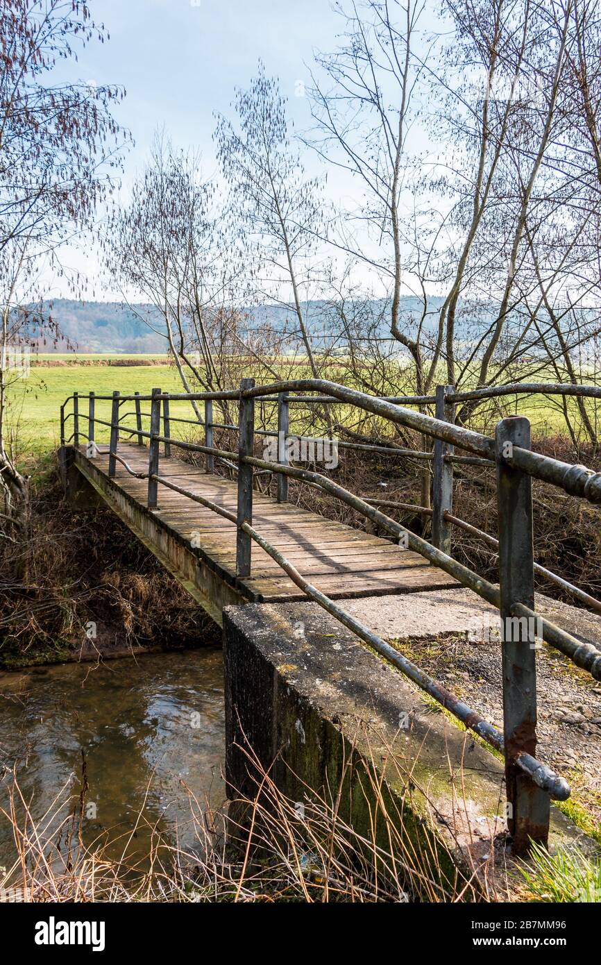 Kleine Eisenbrücke über den kleinen Fluss und eine grüne Wiese Stockfoto