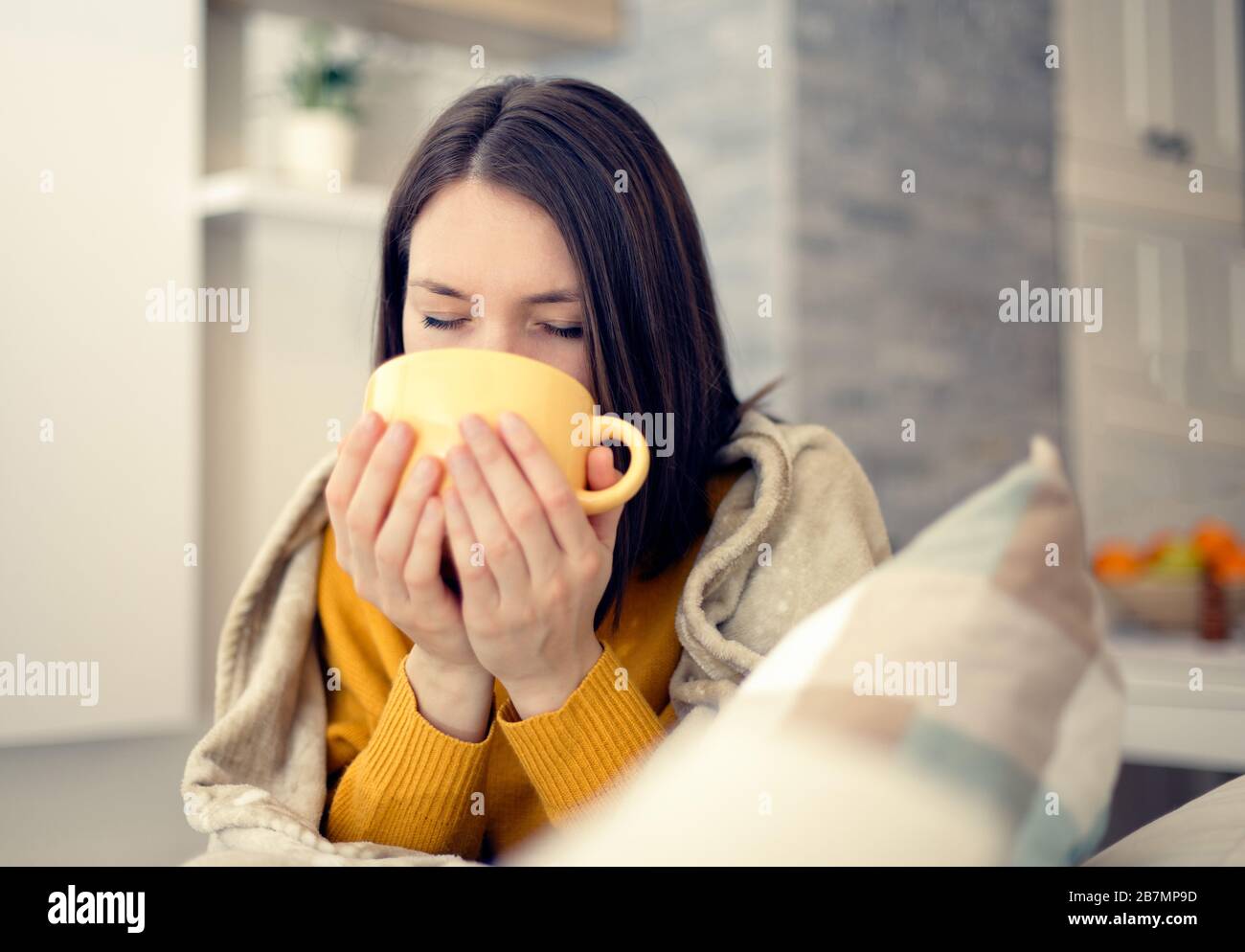 Kranke junge Frau mit Grippevirus zu Hause, die Tee mit Decke trinkt Stockfoto