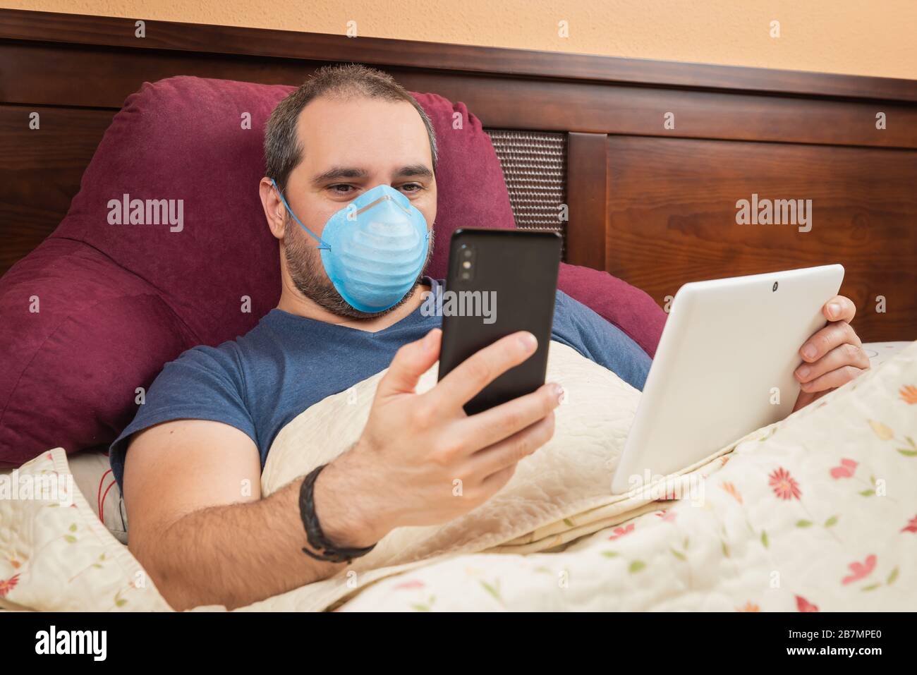 Kranker Mann mit Tablet und Telefon im Bett. Telearbeit Stockfoto