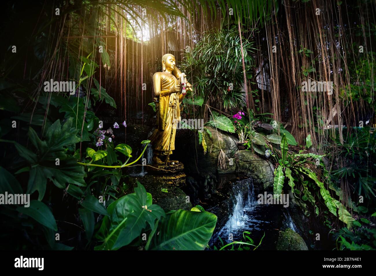 Goldene Buddha-Statue im tropischen Garten mit Wasserfall im Wat Saket goldenen Berg Tempel in Bangkok Stockfoto