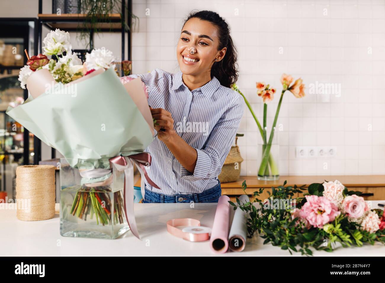 Lächelnder Blumenhändler macht einen Blumenstrauß an der Theke. Junger Unternehmer, der im Blumengeschäft arbeitet. Stockfoto