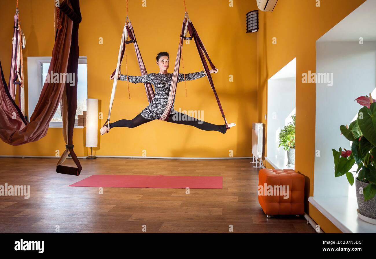 Junge Frau tut Antigravity Yoga Bein split Position im Wellnessstudio mit gelben Wänden Stockfoto