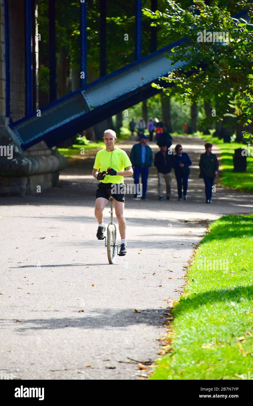 Ein männlicher Unicycler, der in einem leuchtend gelben Oberteil gekleidet ist, der neben dem River Severn im Quarry Park in Shrewsbury radeln kann. Stockfoto