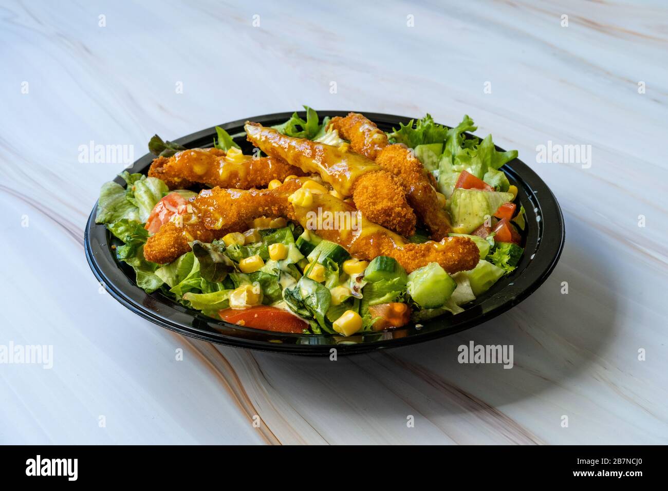 Nehmen Sie gesunden Cajun-Salat mit Hühnchenfingern und Sendesauce in der schwarzen Plastikplatte/Packung weg. Bio Fast Food. Stockfoto
