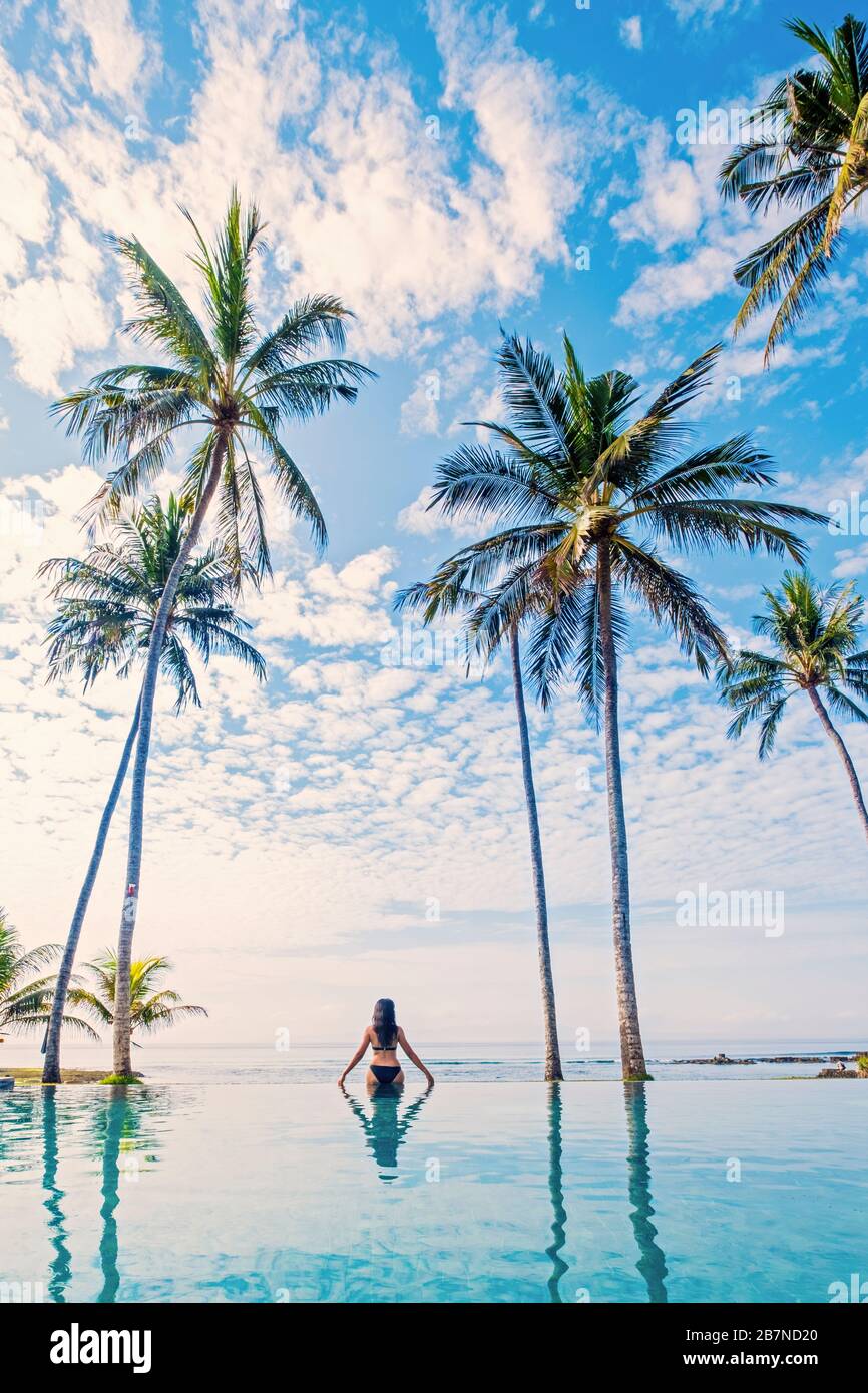Eine junge Frau, die unter Palmen in einem Infinity-Pool steht Stockfoto