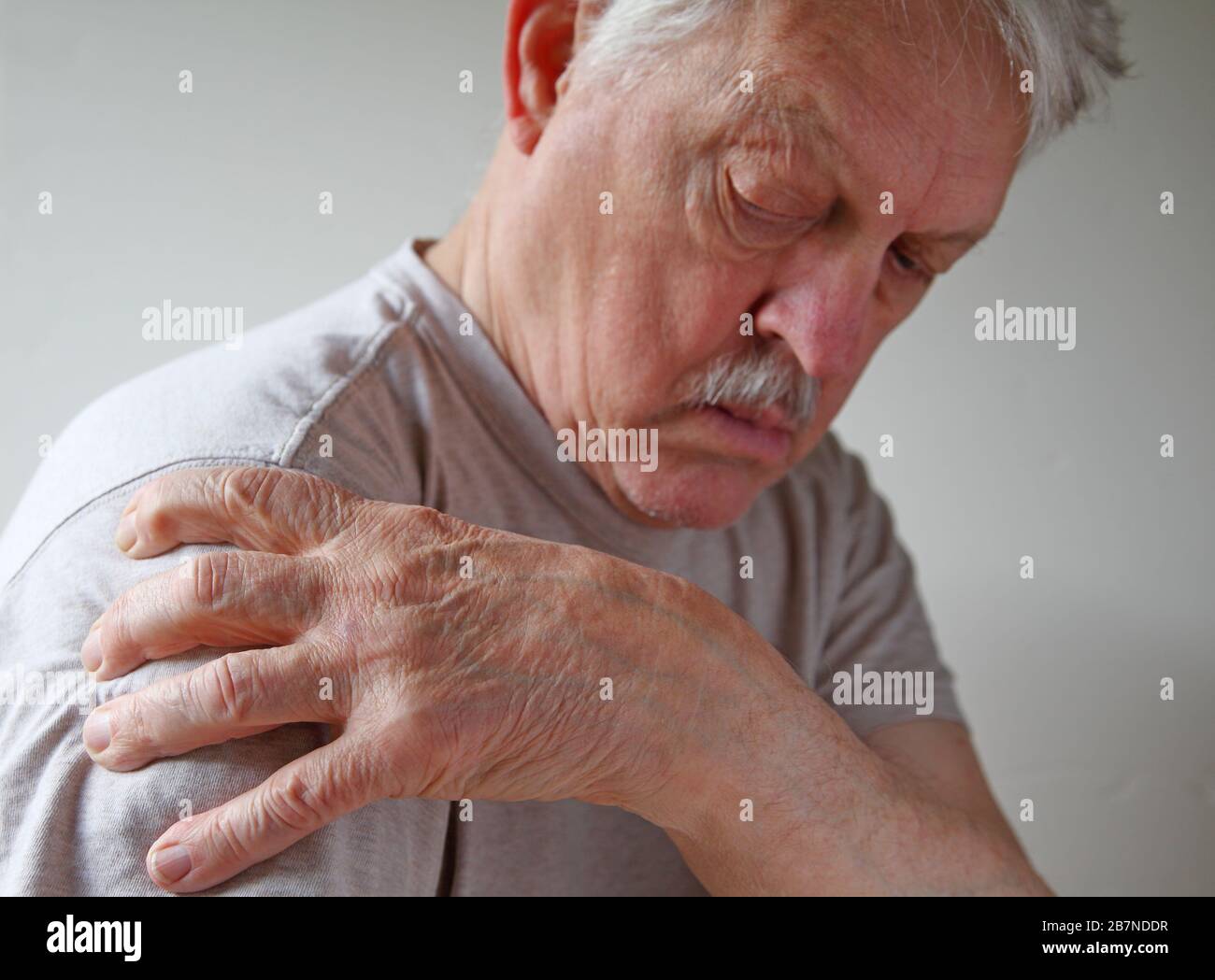 Der ältere Mann greift sich in Schmerzen die Schulter an und hat Platz für Text Stockfoto