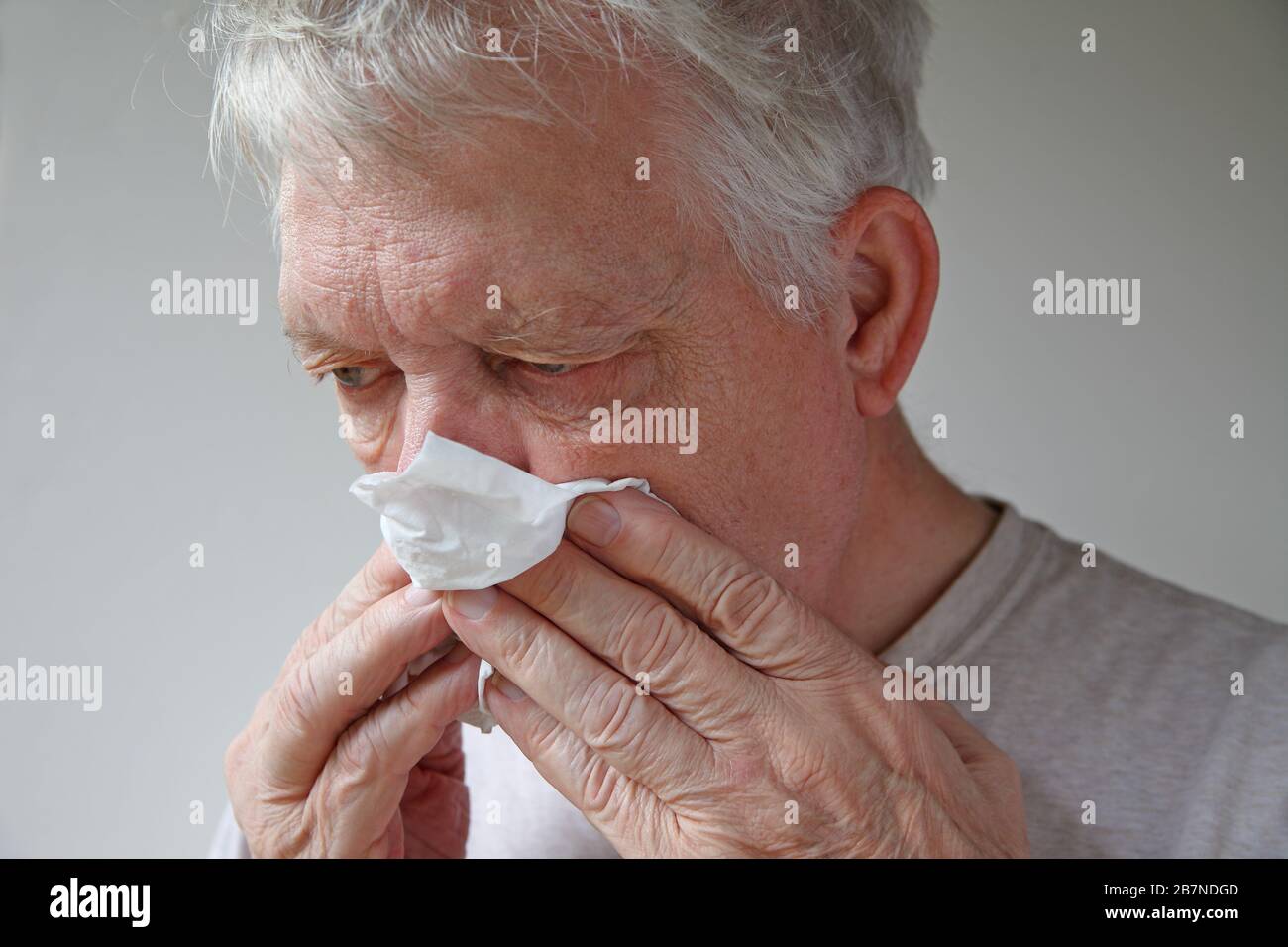 Der ältere Mann verwendet ein Gewebe, um seine Nase zu blasen Stockfoto