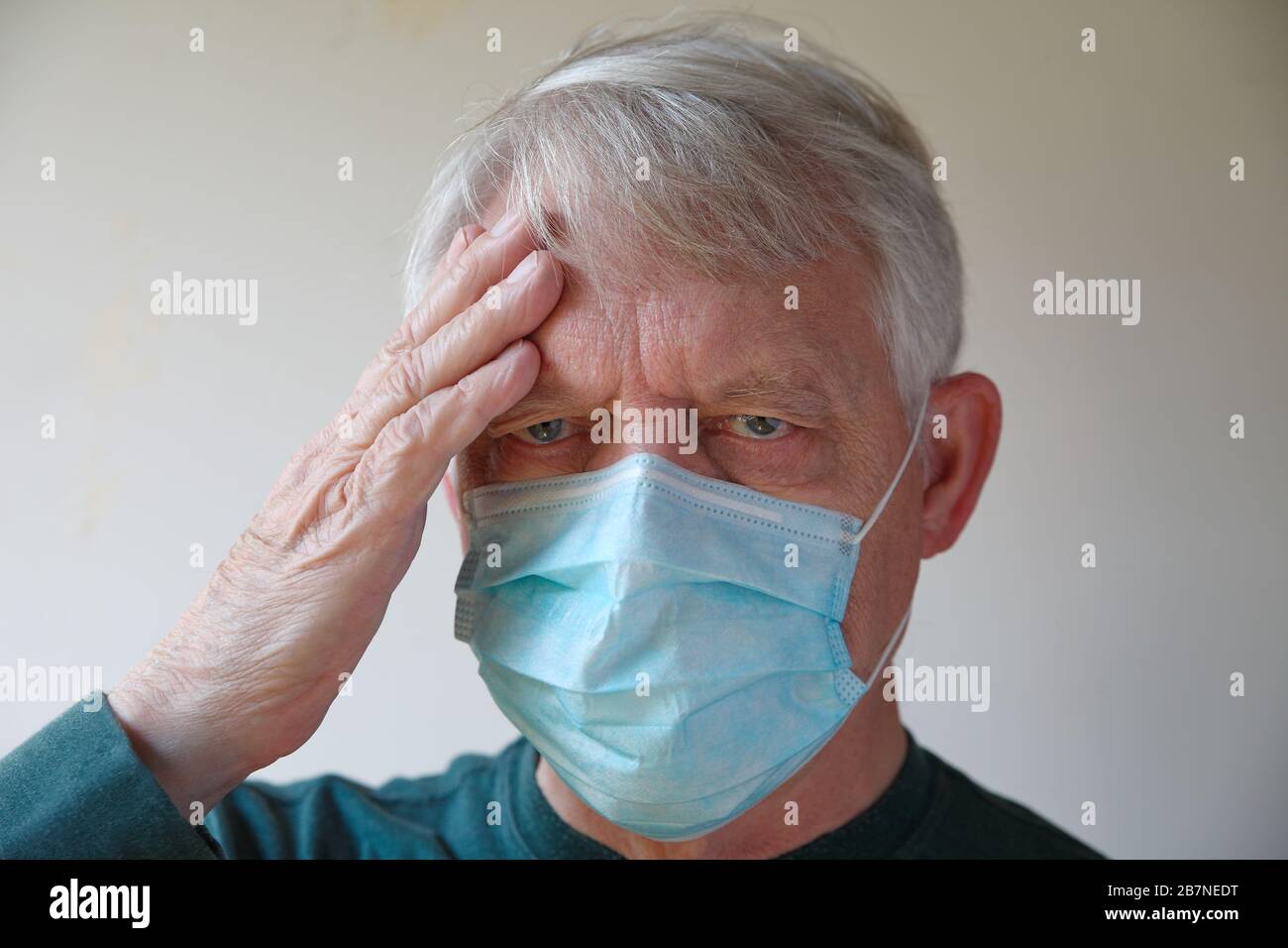 Beim tragen einer Gesichtsmaske hält der ältere Mann eine Hand an der Stirn Stockfoto